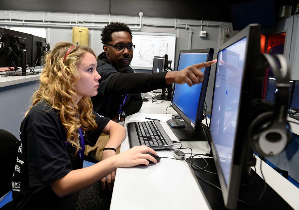Teacher pointing to computer screen in front of student.
Public domain